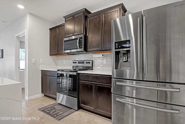 kitchen with stainless steel appliances, backsplash, light stone countertops, light tile patterned flooring, and dark brown cabinetry