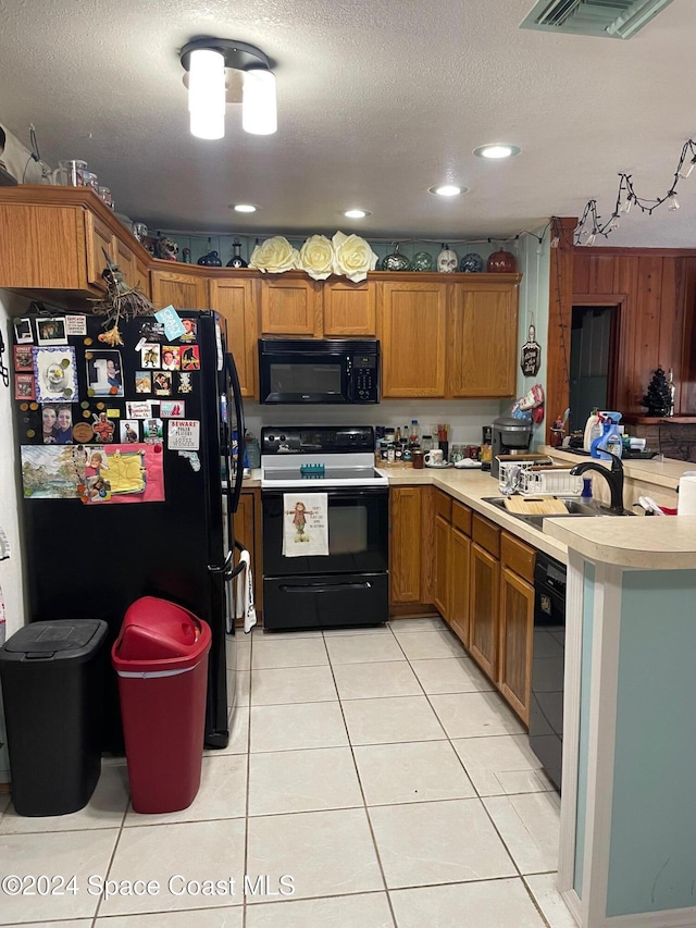 kitchen featuring a textured ceiling, light tile patterned flooring, black appliances, wooden walls, and sink