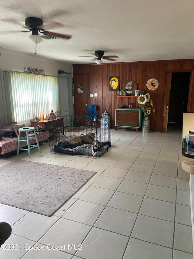 living room featuring ceiling fan, a textured ceiling, light tile patterned floors, and wood walls