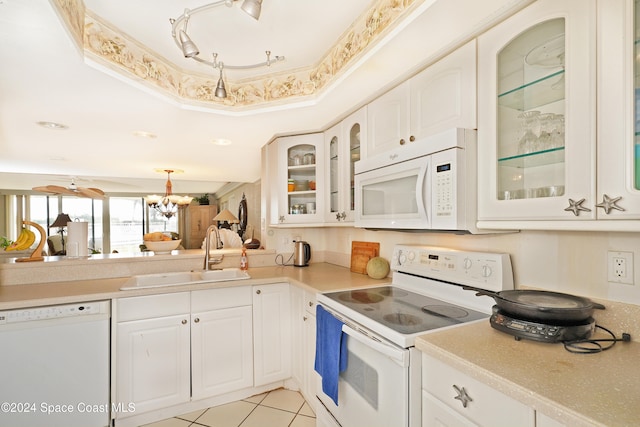 kitchen with white appliances, white cabinets, a raised ceiling, sink, and an inviting chandelier