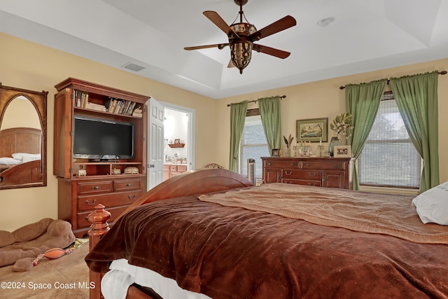 bedroom with tile patterned floors, ensuite bath, a tray ceiling, and ceiling fan