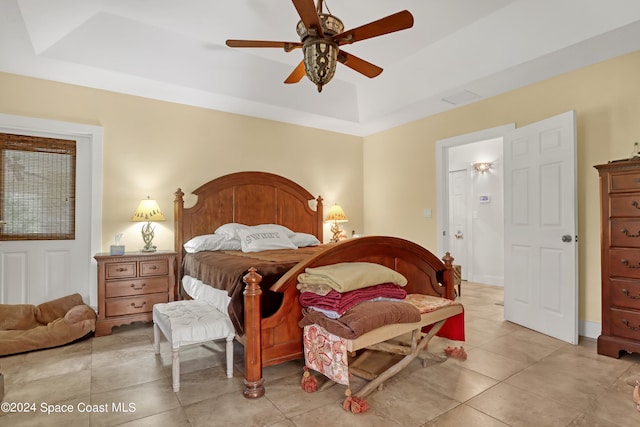 bedroom with a raised ceiling, light tile patterned floors, and ceiling fan