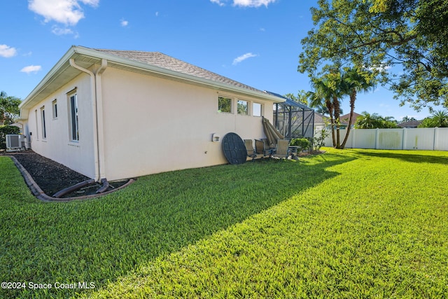 view of side of home with central AC unit, a lanai, and a lawn