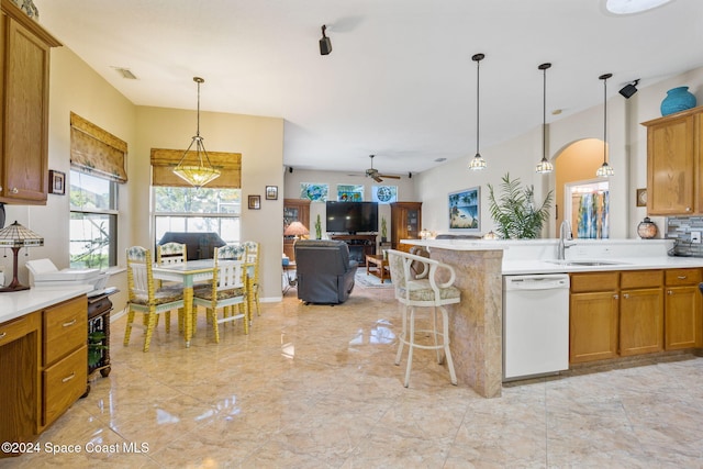 kitchen featuring ceiling fan, sink, white dishwasher, pendant lighting, and a kitchen bar