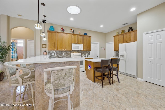 kitchen featuring kitchen peninsula, white appliances, sink, decorative light fixtures, and a breakfast bar area