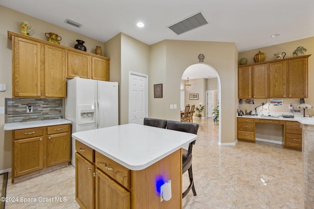 kitchen featuring a kitchen bar, white refrigerator with ice dispenser, a kitchen island, and tasteful backsplash