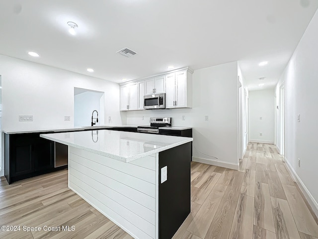 kitchen with kitchen peninsula, white cabinets, appliances with stainless steel finishes, light wood-type flooring, and sink