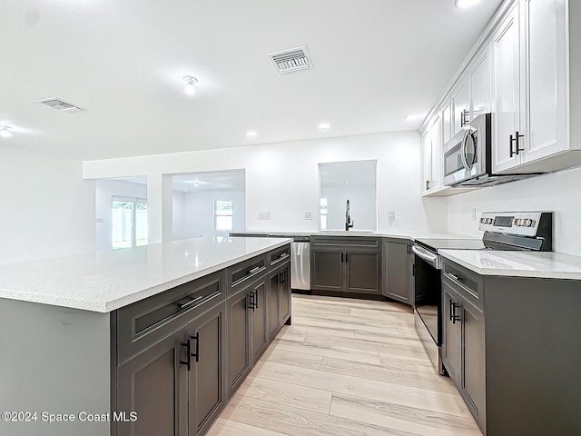 kitchen featuring kitchen peninsula, stainless steel appliances, sink, light wood-type flooring, and white cabinetry