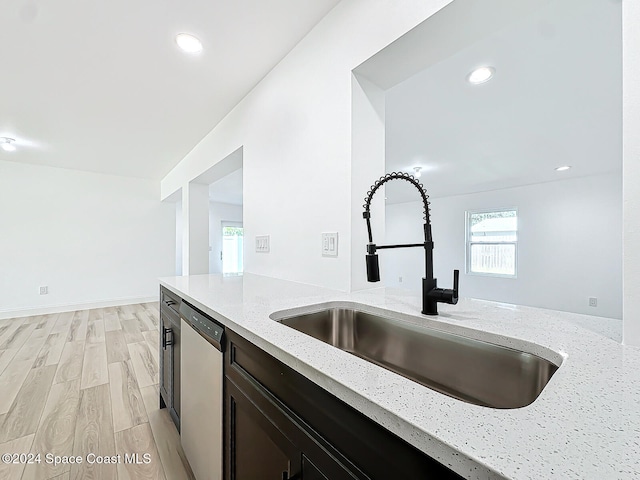 kitchen with stainless steel dishwasher, light hardwood / wood-style flooring, light stone countertops, and sink