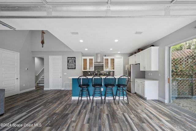 kitchen featuring white cabinets, a breakfast bar, a kitchen island with sink, dark wood-type flooring, and stainless steel refrigerator with ice dispenser