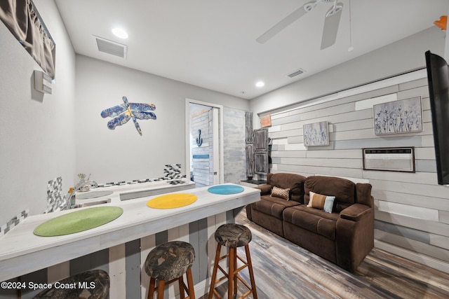 living room with a wall mounted air conditioner, wood-type flooring, and ceiling fan