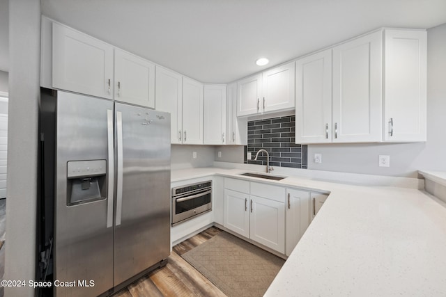 kitchen with appliances with stainless steel finishes, sink, white cabinets, hardwood / wood-style flooring, and decorative backsplash