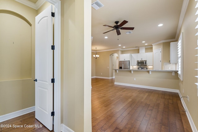 kitchen with stainless steel appliances, hardwood / wood-style flooring, kitchen peninsula, a kitchen breakfast bar, and white cabinets