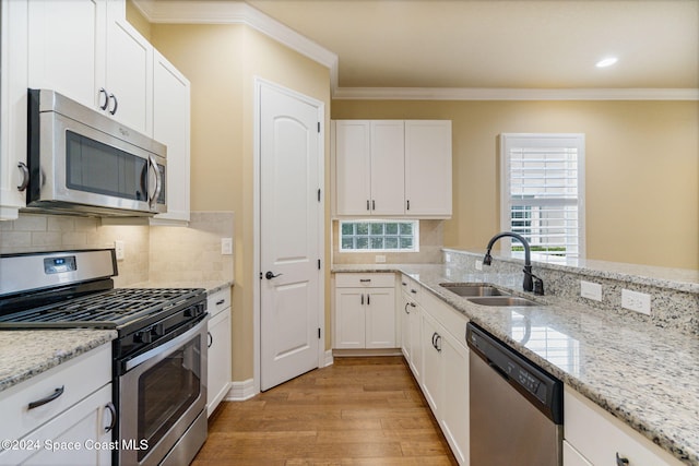 kitchen with appliances with stainless steel finishes, light stone countertops, sink, white cabinets, and light hardwood / wood-style flooring