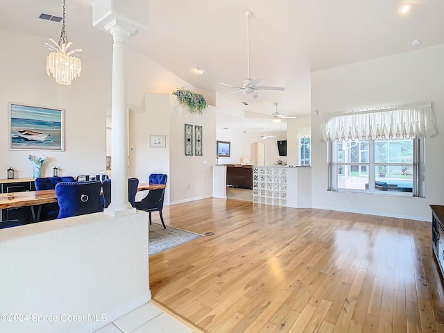 living room featuring ornate columns, hardwood / wood-style flooring, high vaulted ceiling, and ceiling fan with notable chandelier