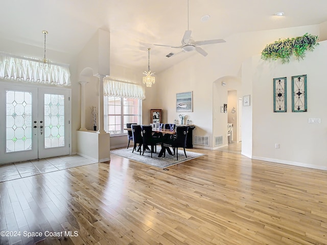 dining area featuring light hardwood / wood-style flooring, french doors, high vaulted ceiling, and ceiling fan with notable chandelier