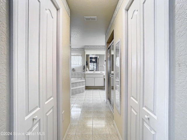 hall with sink, light tile patterned flooring, and a textured ceiling