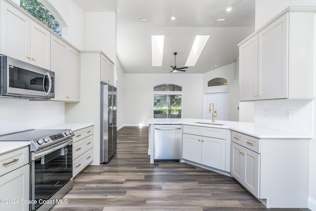 kitchen with dark wood-type flooring, kitchen peninsula, sink, white cabinets, and appliances with stainless steel finishes