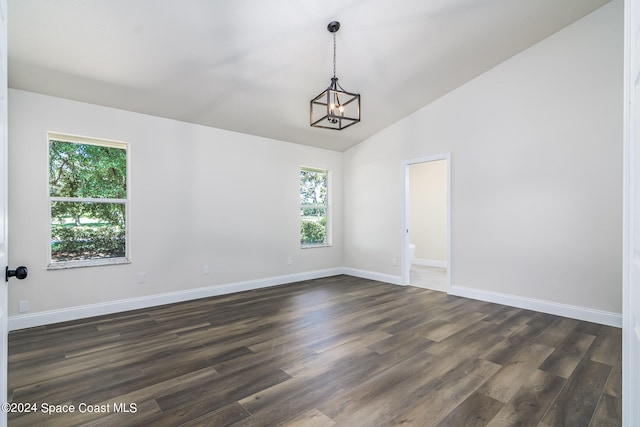 empty room featuring a wealth of natural light, lofted ceiling, dark wood-type flooring, and a chandelier