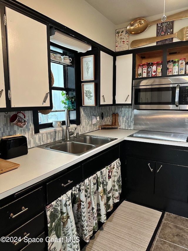 kitchen featuring tasteful backsplash, sink, white cabinets, tile patterned flooring, and black stovetop