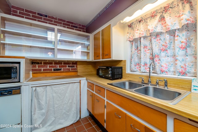 kitchen with dishwasher, stainless steel microwave, sink, dark tile patterned floors, and brick wall