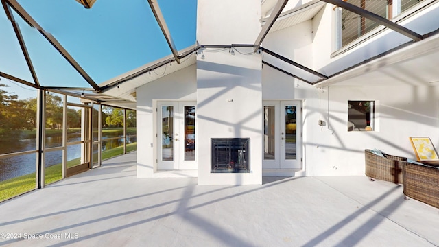 exterior space with a water view, a patio area, french doors, and glass enclosure