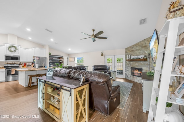 living room with ceiling fan, high vaulted ceiling, wood-type flooring, and a fireplace