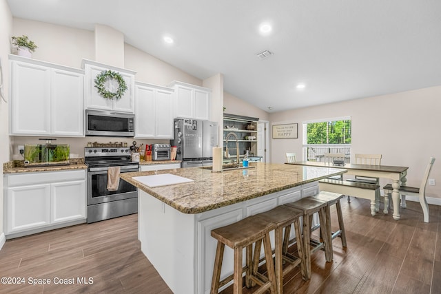 kitchen with a center island with sink, appliances with stainless steel finishes, white cabinetry, hardwood / wood-style flooring, and vaulted ceiling