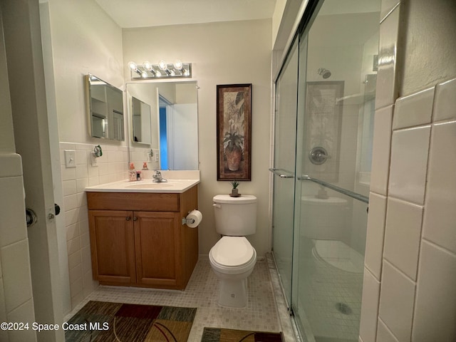 bathroom with a shower with shower door, toilet, tile patterned floors, tile walls, and vanity