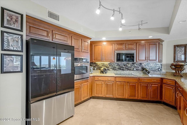 kitchen with tasteful backsplash, a textured ceiling, appliances with stainless steel finishes, a tray ceiling, and light stone counters