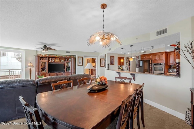 tiled dining room featuring sink, ceiling fan with notable chandelier, and a textured ceiling