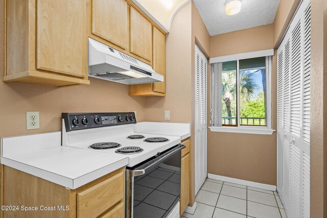 kitchen with a textured ceiling, light brown cabinetry, light tile patterned floors, and white range with electric stovetop