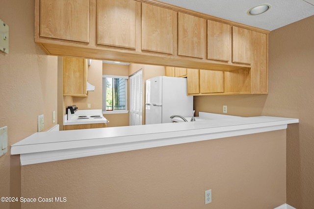 kitchen featuring light brown cabinets, a textured ceiling, and white appliances