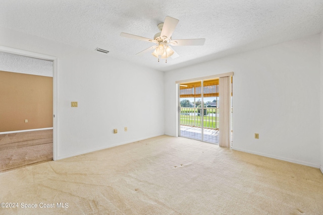 spare room with a textured ceiling, light colored carpet, and ceiling fan