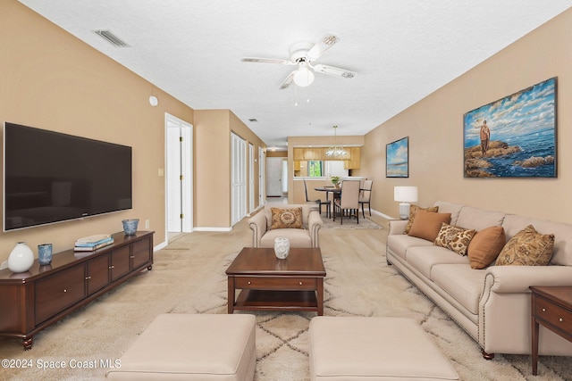 carpeted living room featuring a textured ceiling and ceiling fan with notable chandelier