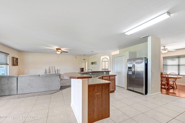 kitchen with stainless steel refrigerator with ice dispenser, a textured ceiling, sink, an island with sink, and light tile patterned floors