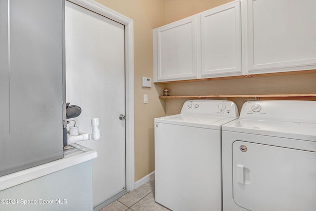 clothes washing area featuring cabinets, light tile patterned flooring, and washer and clothes dryer