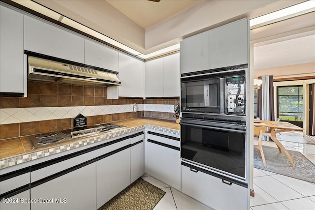 kitchen featuring range hood, black appliances, light tile patterned flooring, white cabinets, and tasteful backsplash