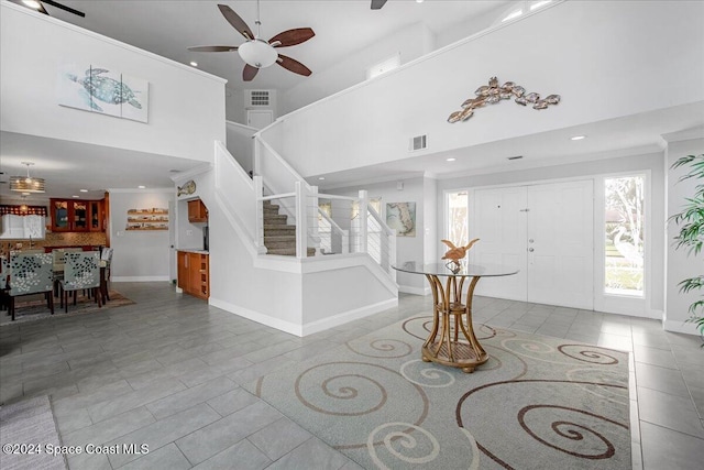 foyer entrance featuring ceiling fan, a towering ceiling, light tile patterned floors, and ornamental molding