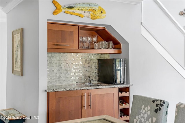 bar with decorative backsplash, light stone countertops, ornamental molding, and sink