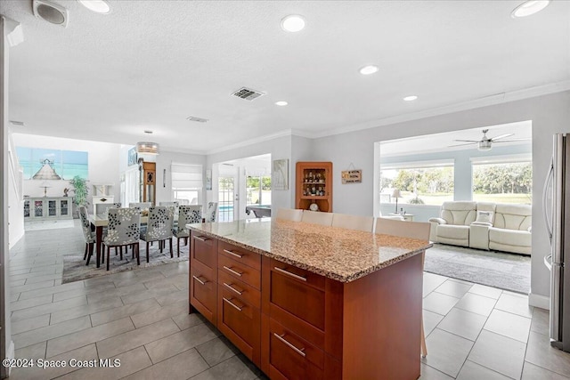 kitchen featuring ceiling fan, a center island, light stone countertops, and crown molding