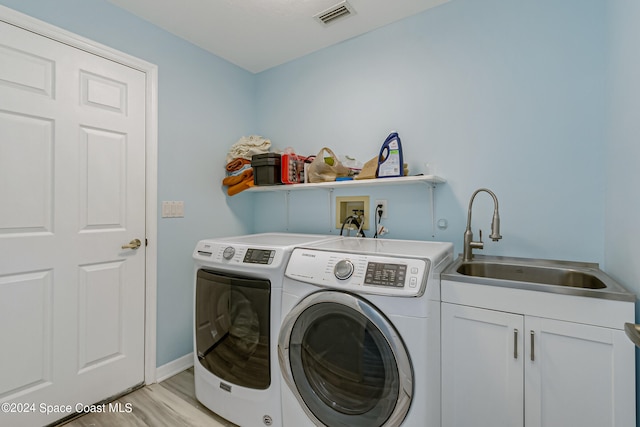 laundry room with sink, light hardwood / wood-style flooring, washer and dryer, and cabinets