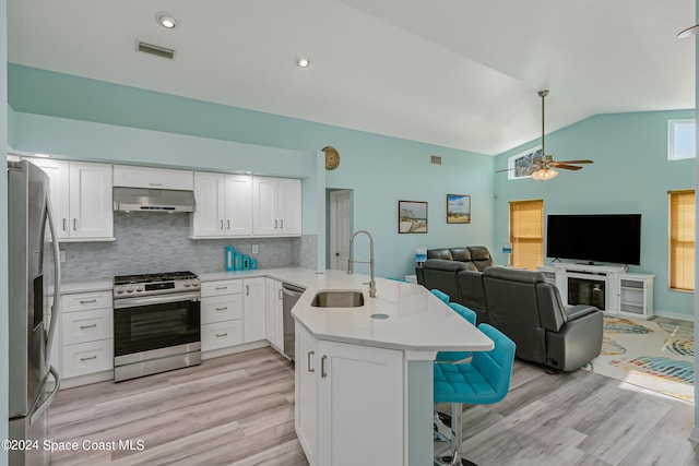 kitchen featuring kitchen peninsula, appliances with stainless steel finishes, white cabinetry, a kitchen bar, and light wood-type flooring