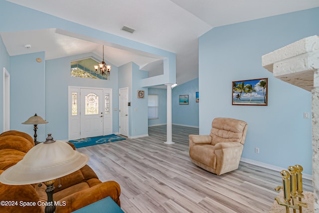 foyer entrance featuring ornate columns, a notable chandelier, lofted ceiling, and light hardwood / wood-style flooring