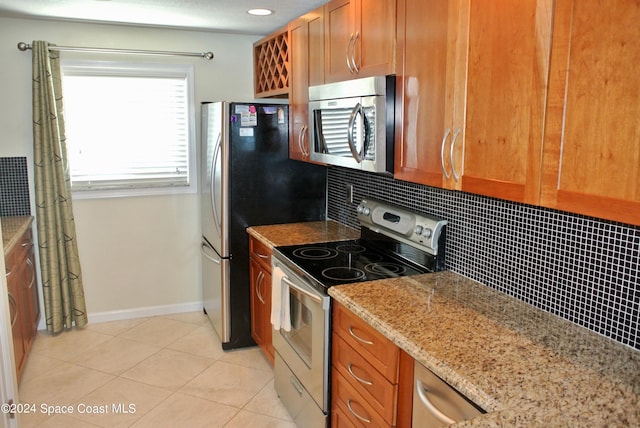 kitchen featuring decorative backsplash, appliances with stainless steel finishes, light stone counters, brown cabinetry, and light tile patterned floors