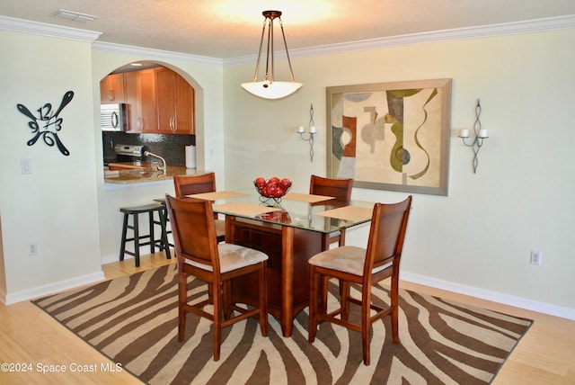dining space featuring arched walkways, light wood-style floors, crown molding, and baseboards