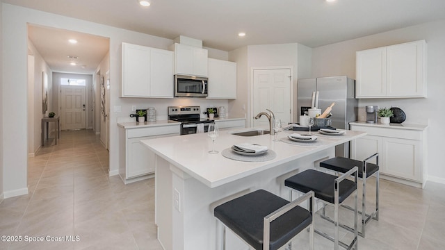 kitchen with sink, appliances with stainless steel finishes, a kitchen island with sink, white cabinets, and a kitchen bar