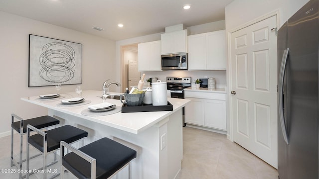 kitchen with white cabinetry, stainless steel appliances, a kitchen bar, and an island with sink