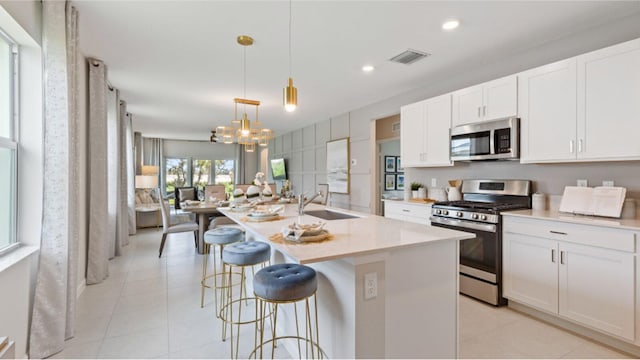 kitchen with an island with sink, hanging light fixtures, sink, white cabinetry, and appliances with stainless steel finishes