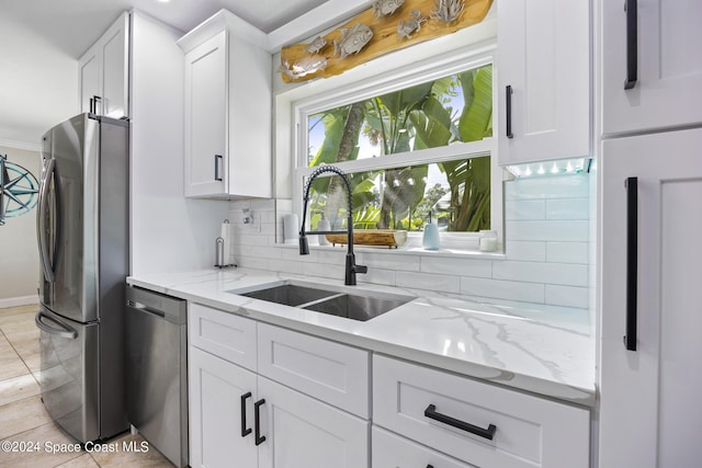 kitchen featuring light stone counters, a sink, white cabinetry, backsplash, and appliances with stainless steel finishes